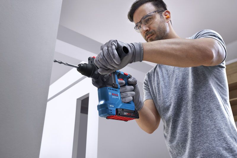 配戴安全設備的人員使用旋轉錘在牆上鑽孔。.