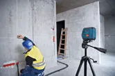一名配戴安全設備的人員正在使用雷射調平工具在牆上做記號。.
