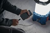一名男子在水泥地面上使用無線工地燈為智慧型手機充電。