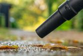 無線吹葉機在雨後清理道路上的濕樹葉。