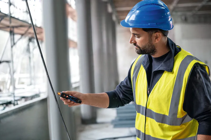 一名配戴安全設備的人員正在使用非接觸式電壓測試器測試電纜。.