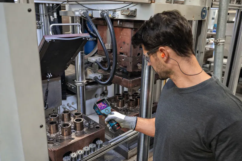 一名配戴安全設備的人員正在使用熱像儀檢查工業機械。.