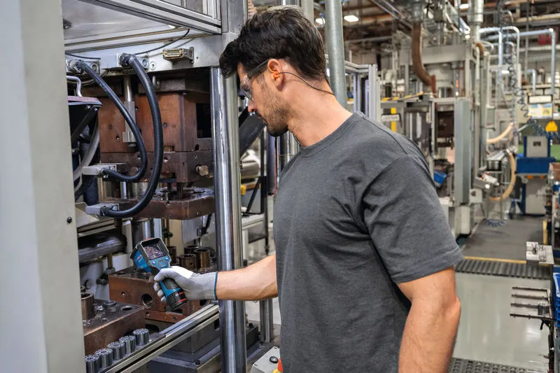 一名配戴安全設備的人員在工廠裡用熱像儀檢查機器。.