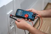 有人使用數位萬用電表檢查牆壁插座的電壓。
