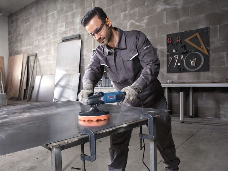 一名佩戴安全設備的人正在用電動工具拋光金屬板。.