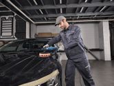 一名配戴安全設備的人員正在使用電動工具擦拭汽車引擎蓋。