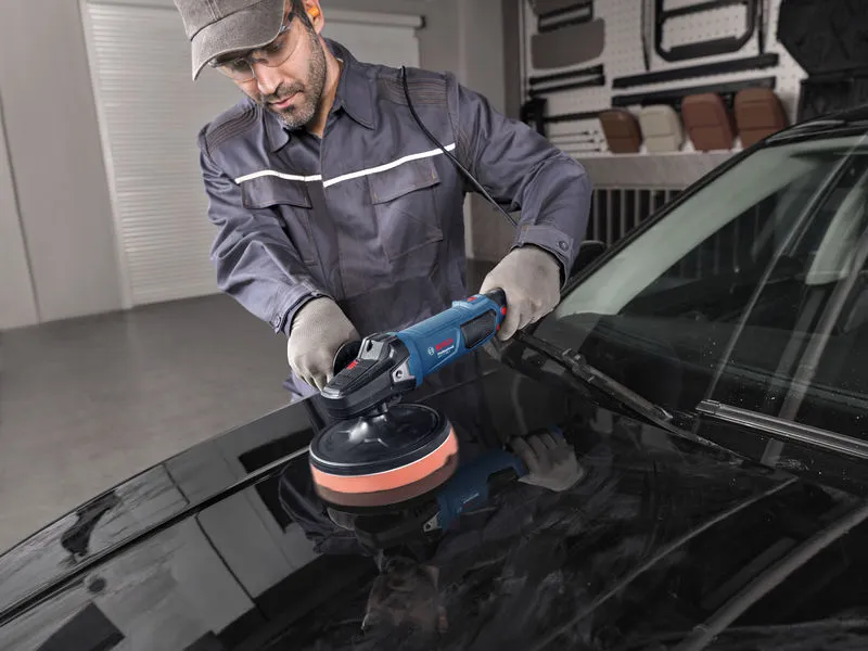 一名佩戴安全設備的人員正在使用電動拋光機拋光汽車引擎蓋。.
