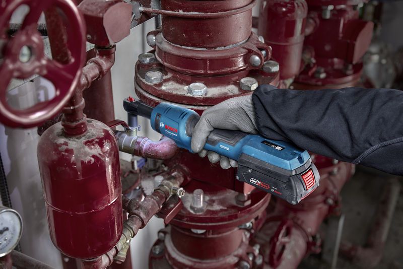 一名佩戴安全設備的人員使用無線棘輪扳手對工業管道進行操作。.