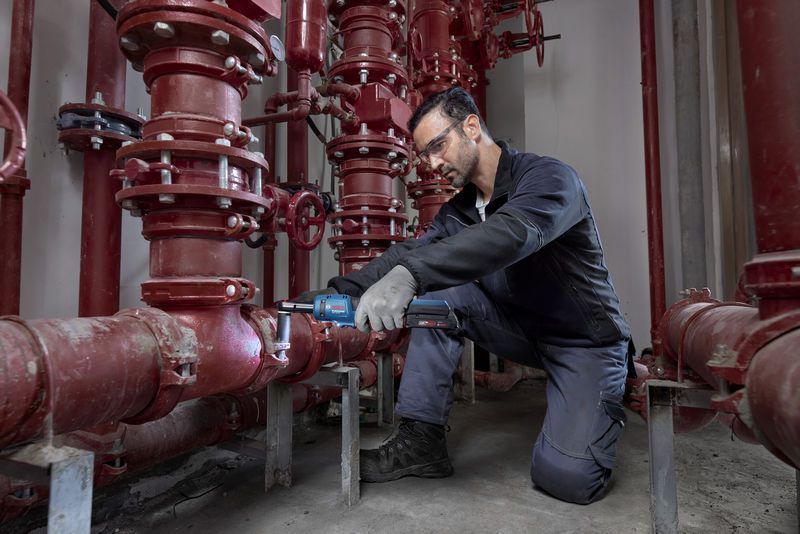 一名配戴安全設備的人員使用無線棘輪扳手操作紅色管道系統。.