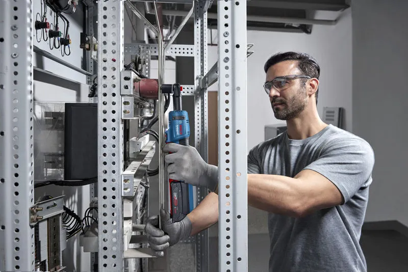 一名配戴安全裝備的人員在金屬架上使用無線棘輪扳手。.