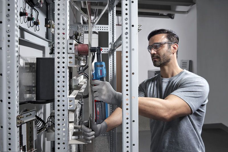 一名配戴安全裝備的人員在金屬架上使用無線棘輪扳手。.