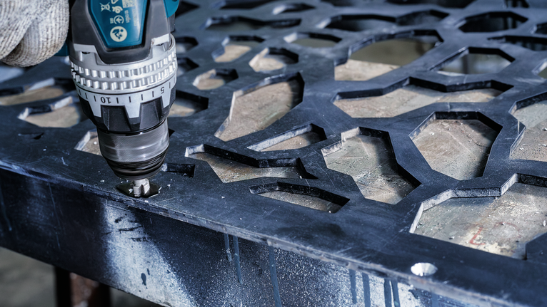 配戴安全設備的人員使用無線電鑽在金屬板上鑽孔。.