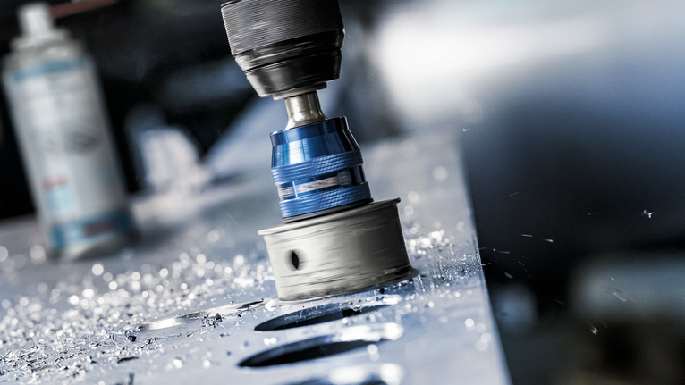 孔鋸在金屬板上鑽出圓形孔，周圍散落著金屬屑。