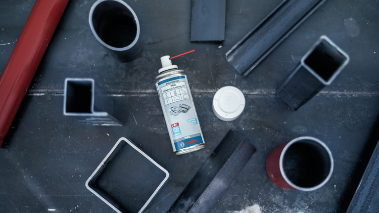 噴霧罐放置在金屬工作台上，周圍環繞著各種鋼管。