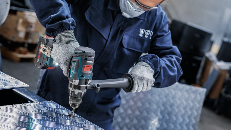 一名配戴安全設備的人員正在一塊有圖案的金屬板上鑽孔。