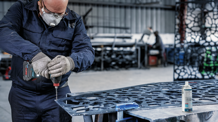 一名配戴安全設備的人員在車間使用電動工具鑽金屬。