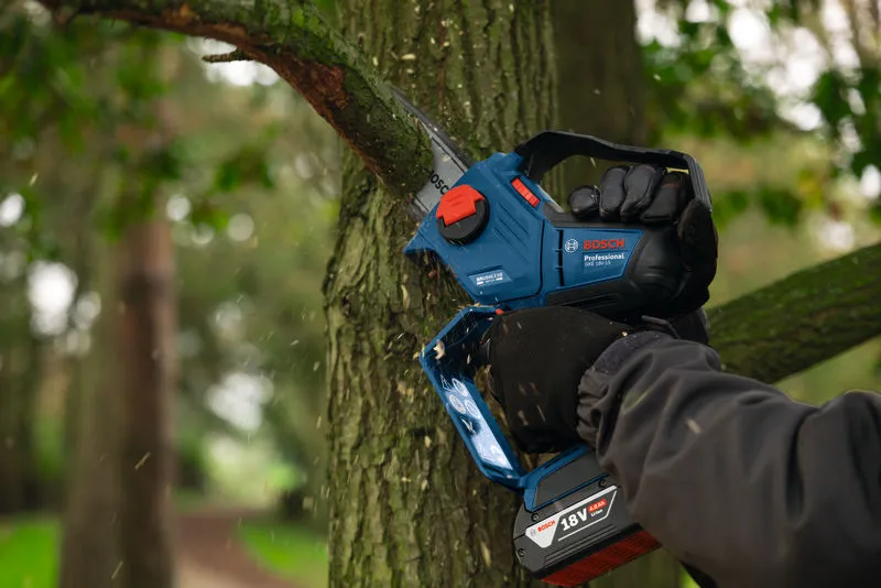 一名佩戴安全裝備的人正在使用無線修枝鋸修剪樹枝。.