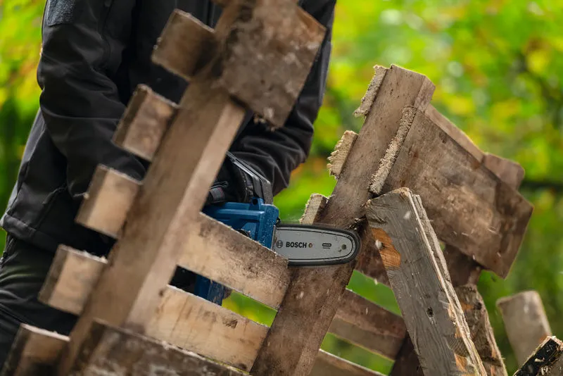 一名配戴安全設備的人員正在使用無線修枝鋸切割木板。.