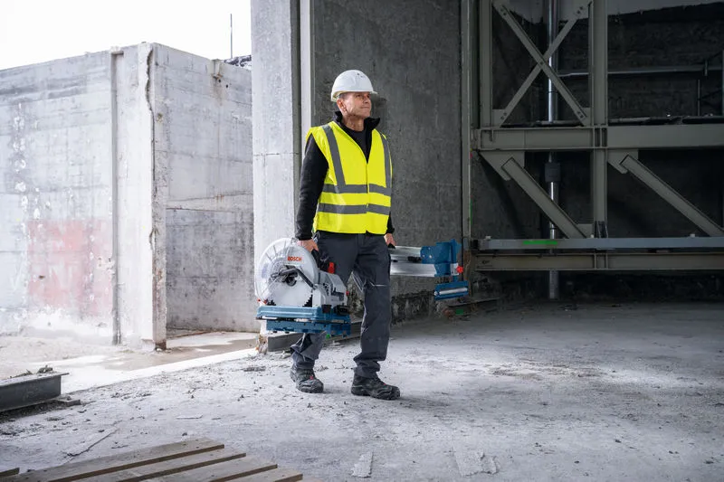 一名配戴安全設備的人員在一棟未完工的建築物內攜帶一把金屬切割鋸。.