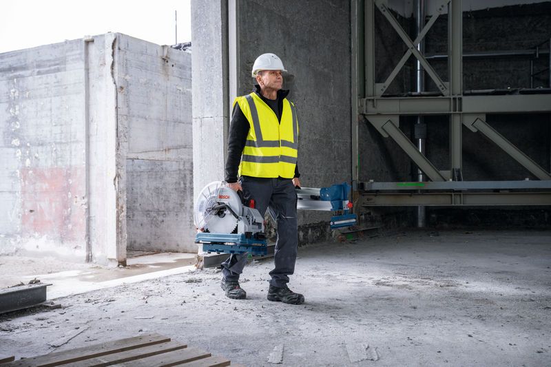 一名配戴安全設備的人員在一棟未完工的建築物內攜帶一把金屬切割鋸。.