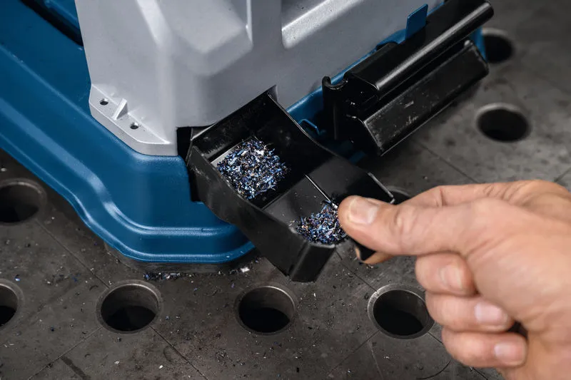 一個人正在清空工作台上的金屬切割鋸中的金屬碎屑托盤。.