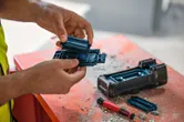 一名配戴安全設備的人員在佈滿灰塵的工作台上更換電動工具的電池。.