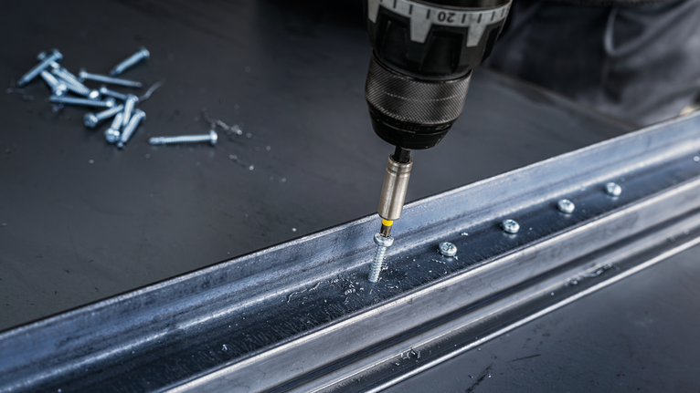 電鑽將螺絲旋入工作台上的金屬梁。