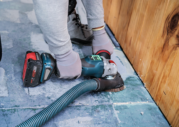 一名配戴安全設備的人員正在打磨木牆附近的混凝土地板。.