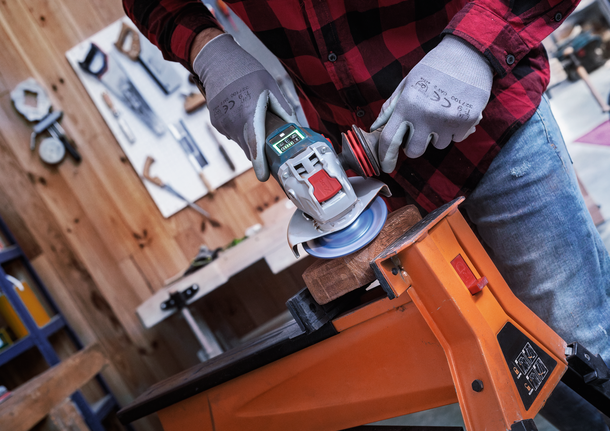 配戴安全設備的人員使用角磨機打磨夾在工作台上的木材。.