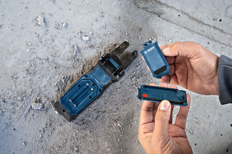 一名工人在佈滿灰塵的水泥地板上更換電動工具底座中的電池。.