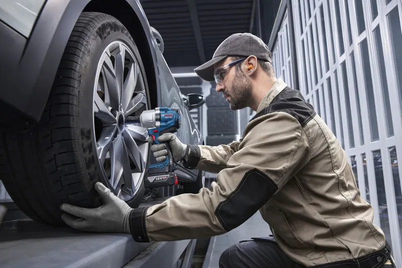 一名配戴安全設備的人員使用無線衝擊扳手來擰緊車輪。.