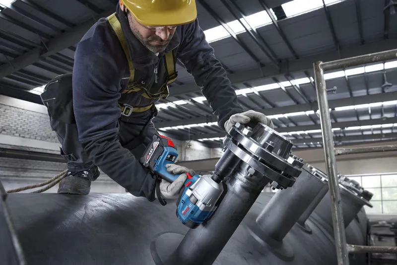 一名佩戴安全設備的人員使用無線衝擊扳手對工業管道進行操作。.