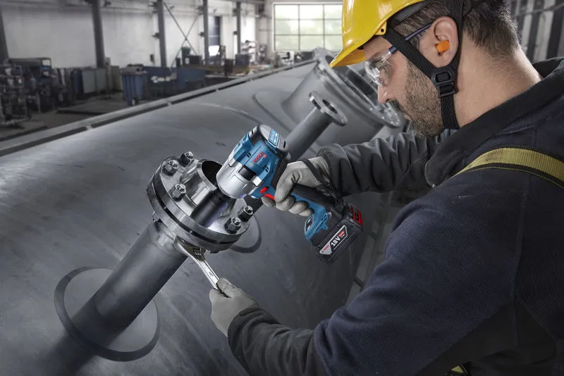 一名配戴安全設備的人員使用無線衝擊扳手來擰緊工業管道上的螺栓。.