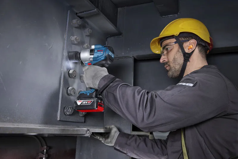 一名配戴安全設備的人員使用無線衝擊扳手來擰緊鋼樑上的螺栓。.