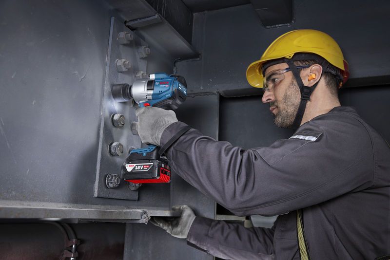 一名配戴安全設備的人員使用無線衝擊扳手來擰緊鋼樑上的螺栓。.