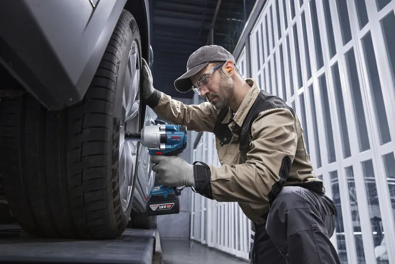 一名配戴安全設備的人使用無線衝擊扳手來擰緊車輪。.