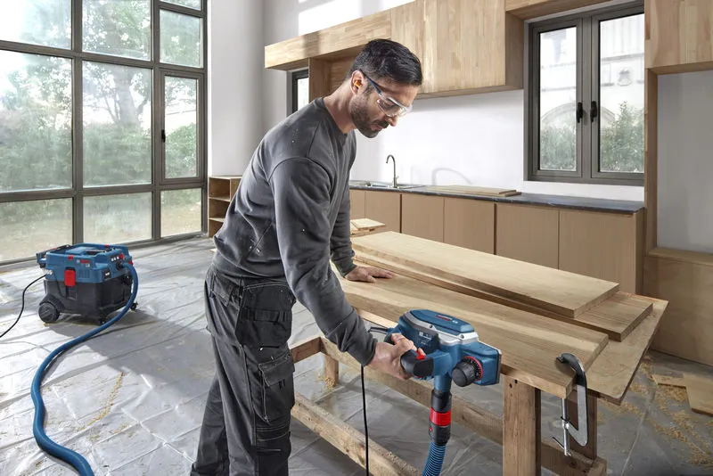 一名佩戴安全設備的工人在車間使用刨床刨削木板。.