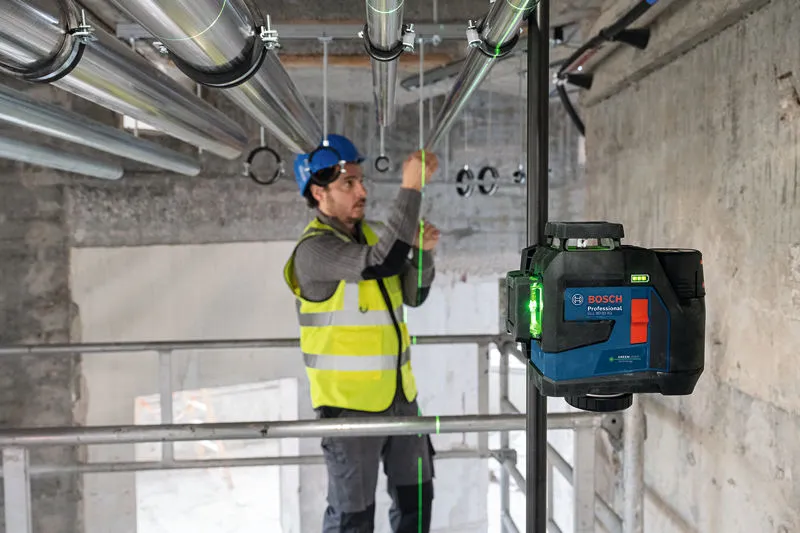 一名配戴安全設備的人員使用雷射調平工具對準管道。.