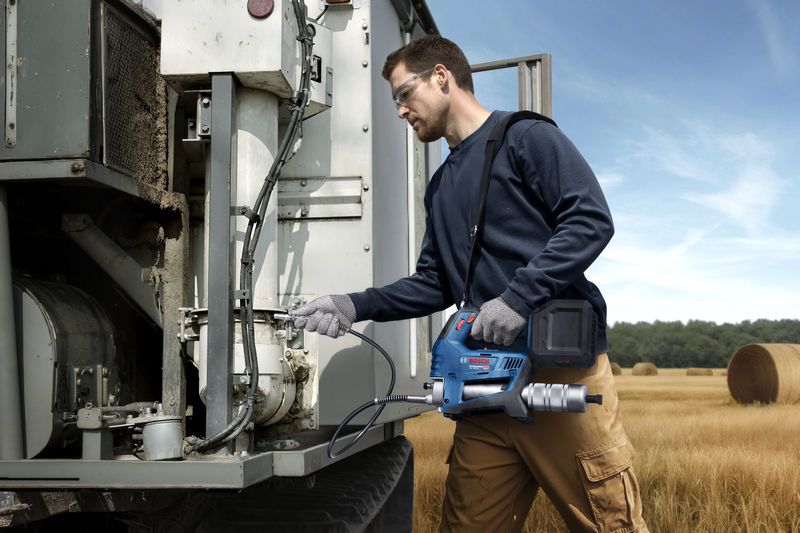 一名配戴安全設備的人員使用無線奶油槍來維修農用機械。.