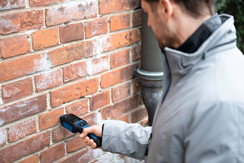 一個人用材料濕度計掃描磚牆。.