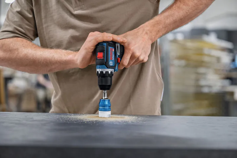 一名男子在黑暗的表面上操作帶有孔鋸附件的無線電鑽。