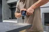 一個人用無線電動工具在工作檯面上鑽孔。