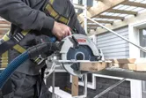 一名配戴安全裝備的人員在鷹架上用無線圓鋸切割木材。.