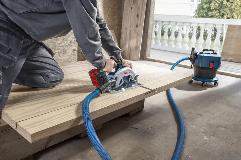 一個人用連接到除塵器的無線圓鋸切割木材。.