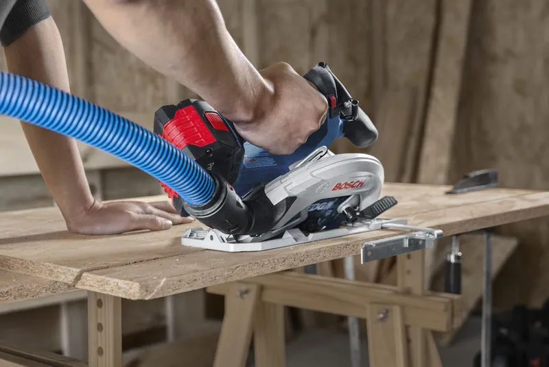 一個人在切割膠合板時引導帶有除塵軟管的無線圓鋸。.
