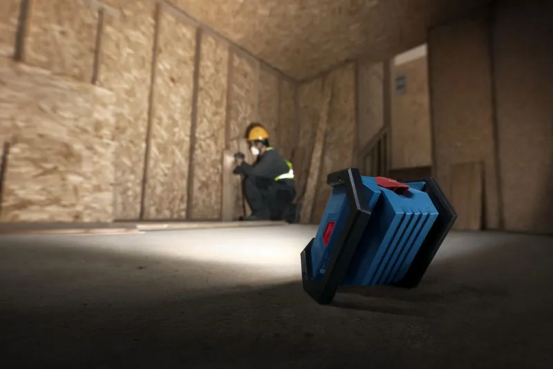 一名佩戴安全設備的人員正在安裝乾牆，現場無線燈為其提供照明。.