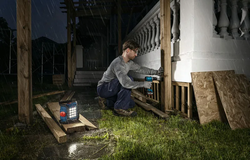 一名身穿安全裝備的人員在夜間用附近的無線工地燈鑽木柱。