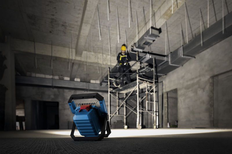 無線工地燈照亮鷹架上配戴安全設備的人員。.