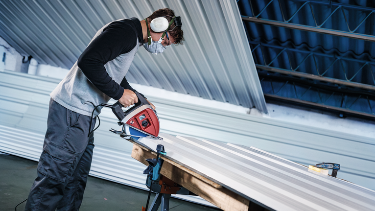 一名穿戴安全裝備的人員正在用電鋸切割金屬板。
