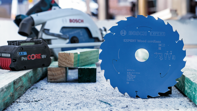 圓鋸片直立在工作台上，旁邊是無線電池和鋸子。.